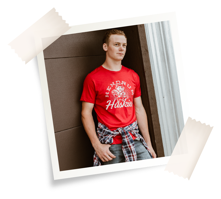 A young man in a red Hendrum Huskies tee leaning against a doorway